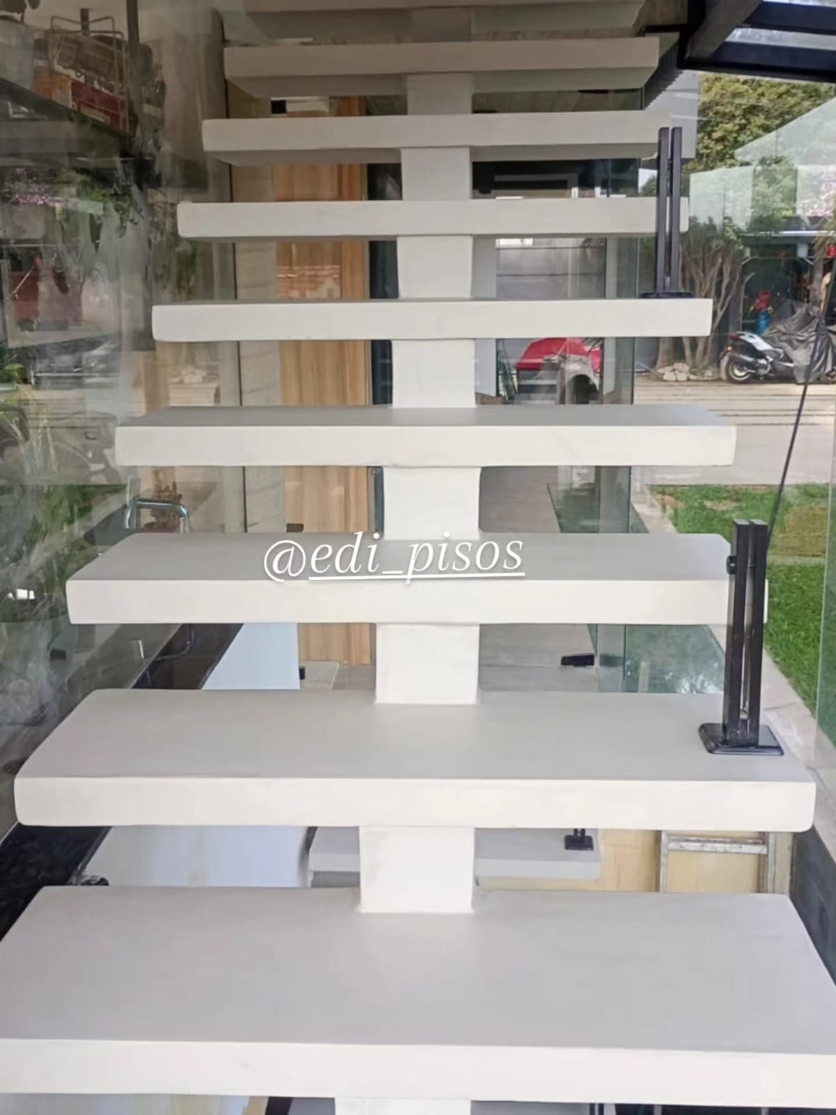Escada flutuante com degraus revestidos em tecnocimento branco, em residência com fechamento de vidro