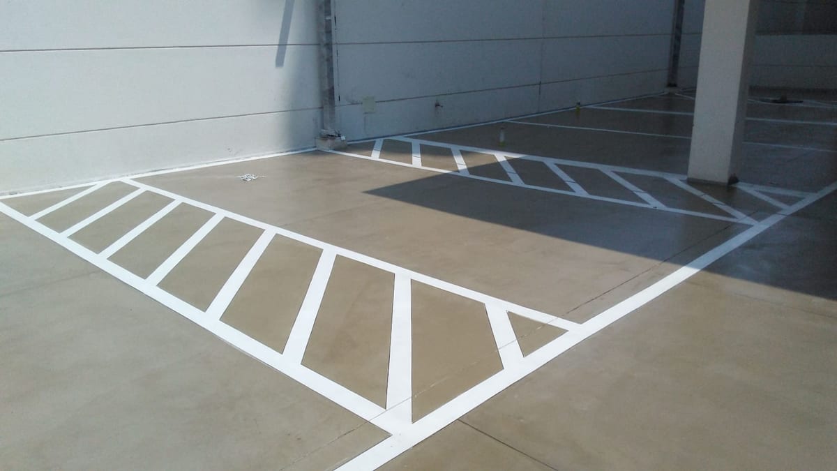 Piso de estacionamento concluído, com faixas brancas de demarcação e zebrado pintados sobre revestimento contínuo