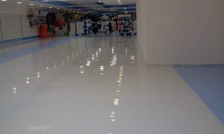 Corredor de galeria comercial com piso autonivelante branco de alto brilho e faixa azul acompanhando a circulação