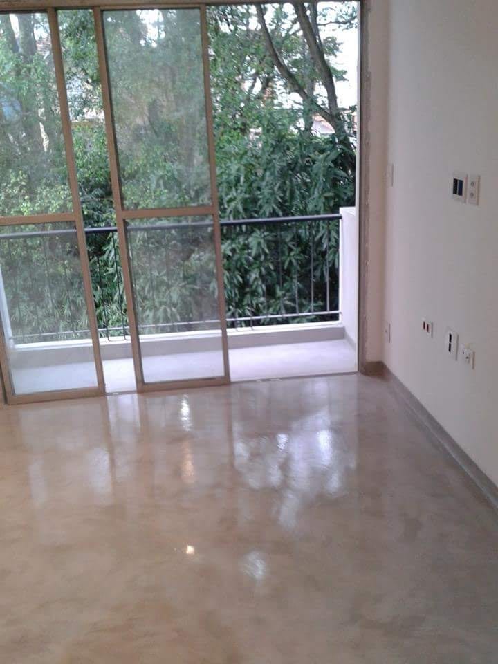 Sala com piso contínuo claro e polido, iluminada por uma porta-janela que dá para a vegetação